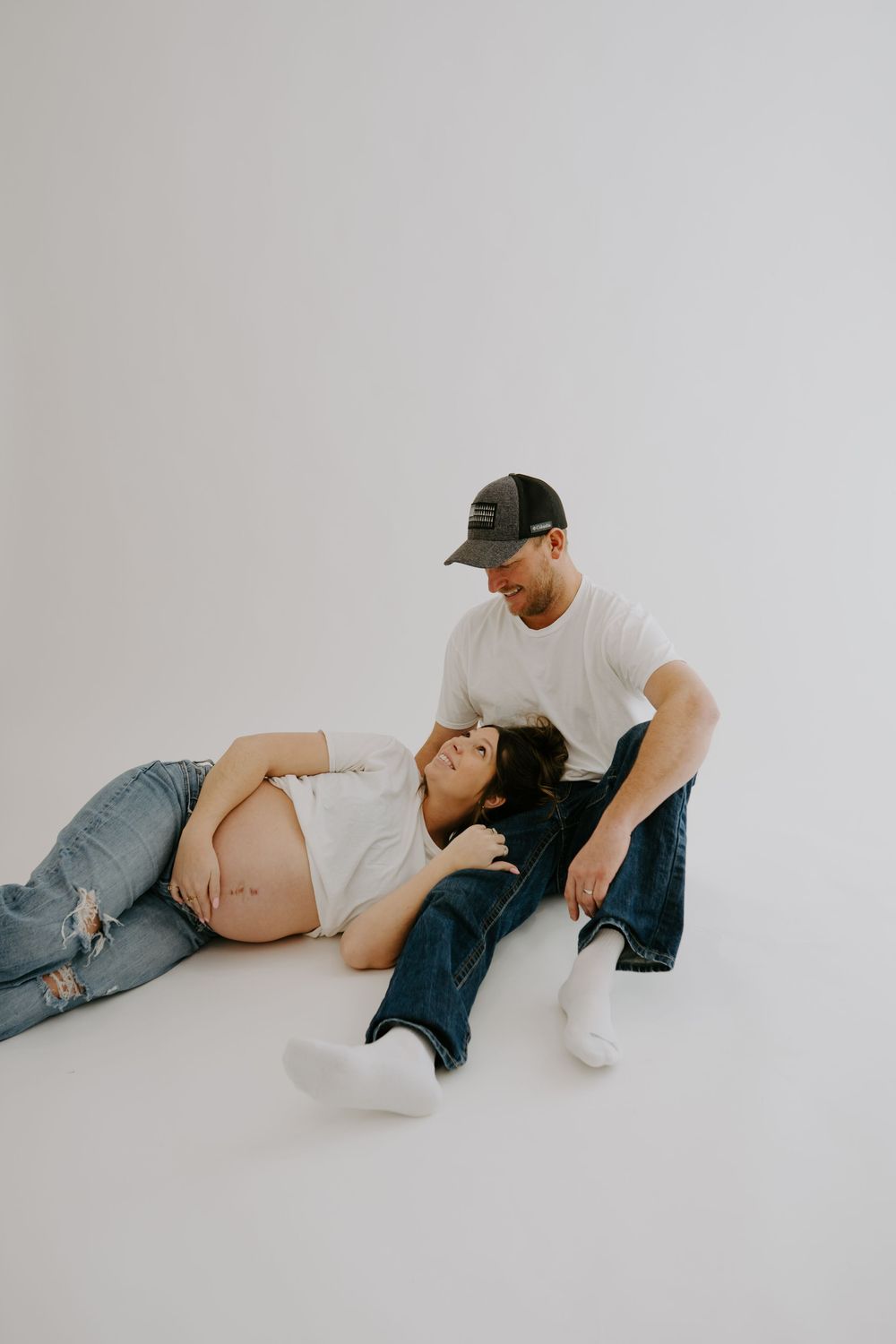 Maternity photo showing couple in casual wear on white background.