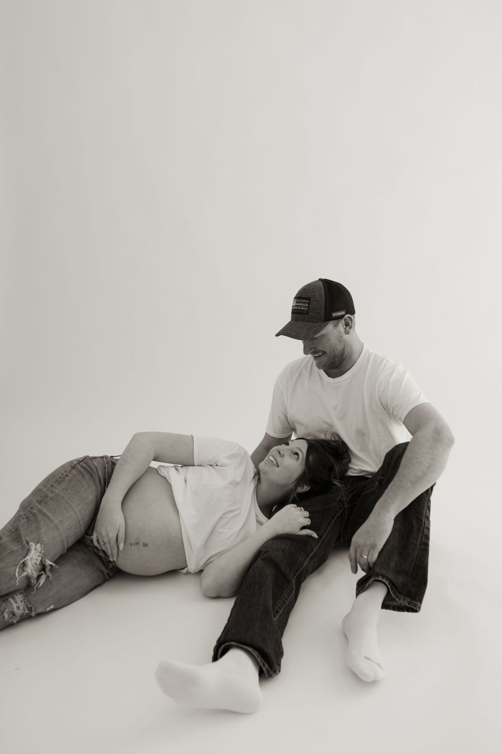Black and white pregnancy photo of couple relaxing on studio floor.