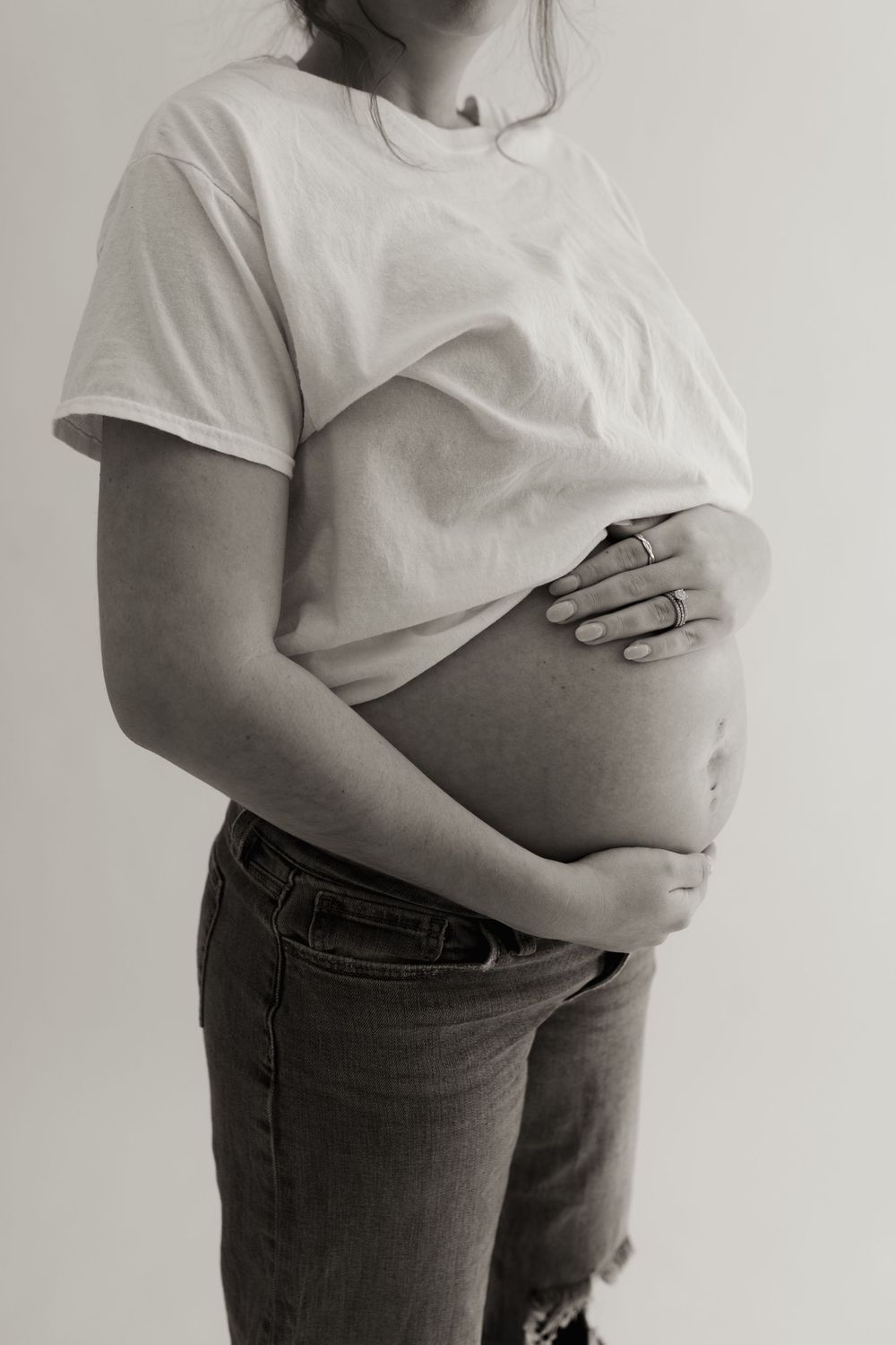 Black and white photo of a pregnant belly in casual attire with hands cradling the bump.