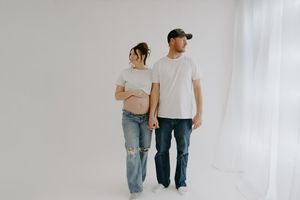 Side view of expectant couple walking together in casual attire against white backdrop.