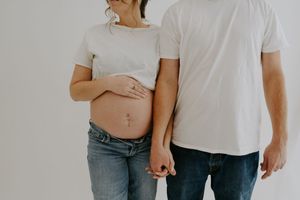 Intimate maternity photo showing couple holding hands with visible baby bump.