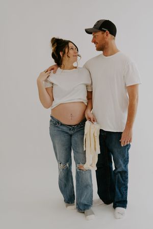 Candid maternity photo of couple sharing intimate moment against white background.