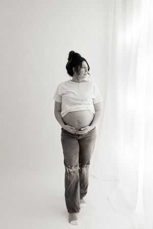 Black and white maternity photo of pregnant woman in distressed jeans and white t-shirt.