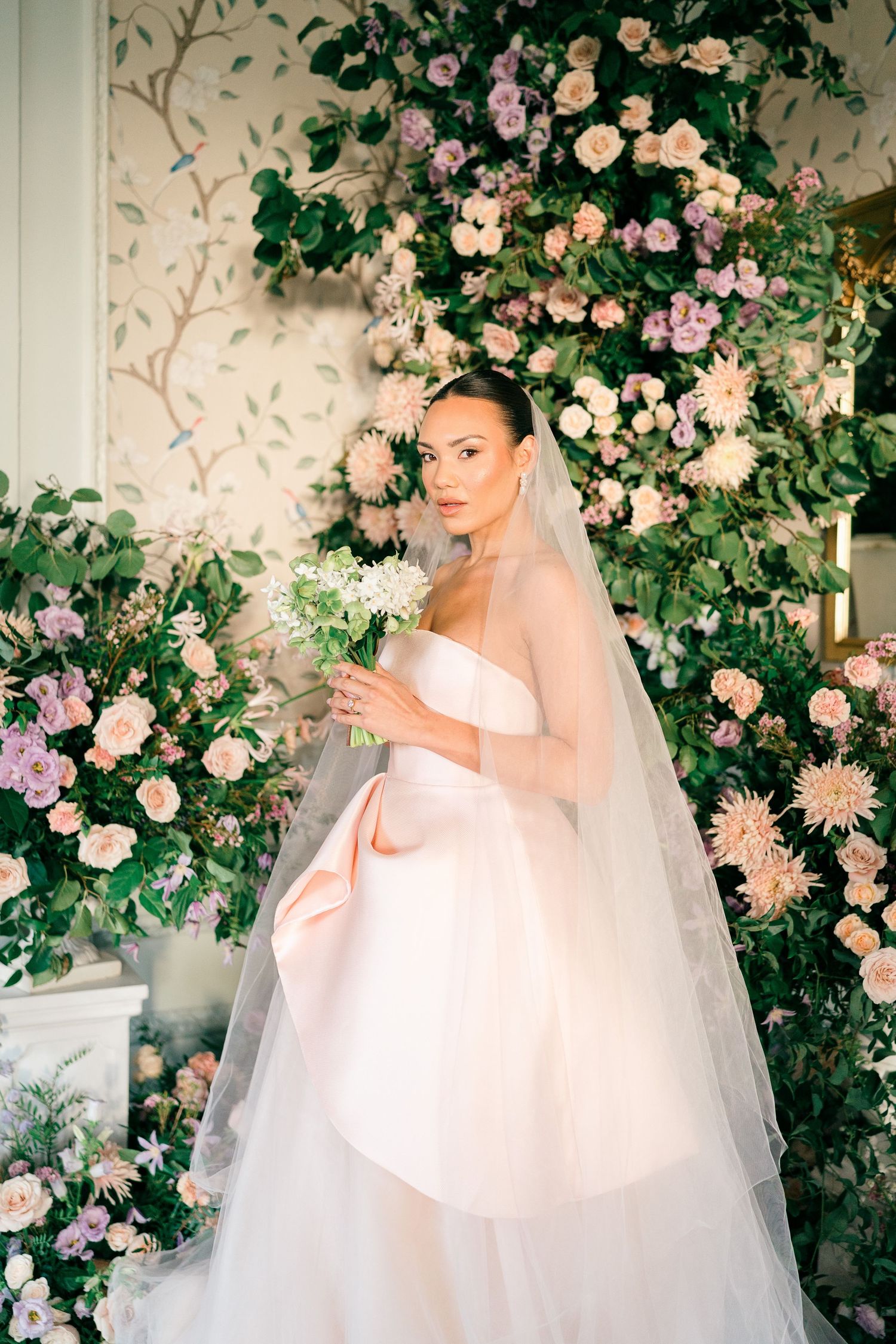 Elegant wedding scene with blush pink roses and floral arrangements surrounding a bride in a classic white gown and veil.