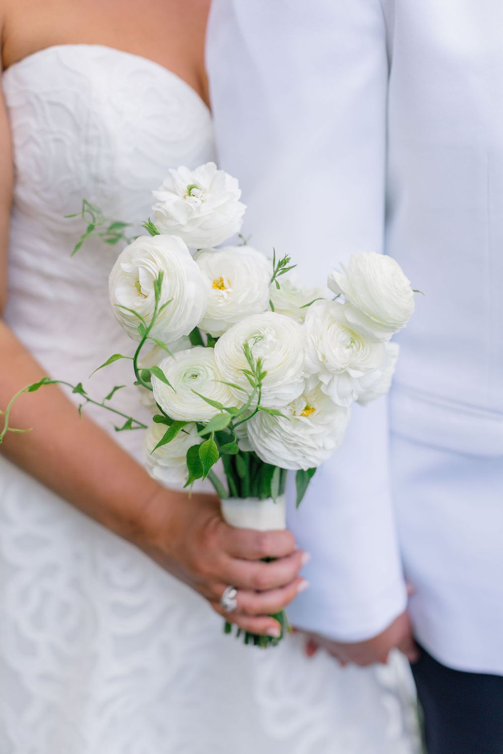 A delicate white ranunculus wedding bouquet held against a white bridal gown.