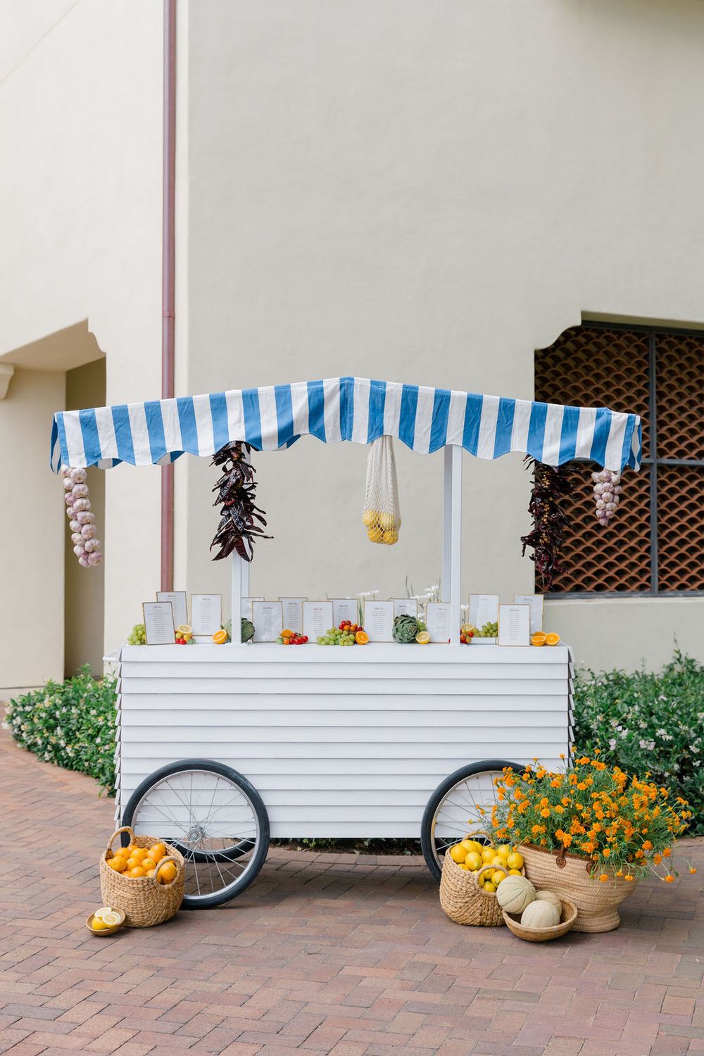 Charming white beverage cart with blue striped awning and fresh produce baskets displayed at base.