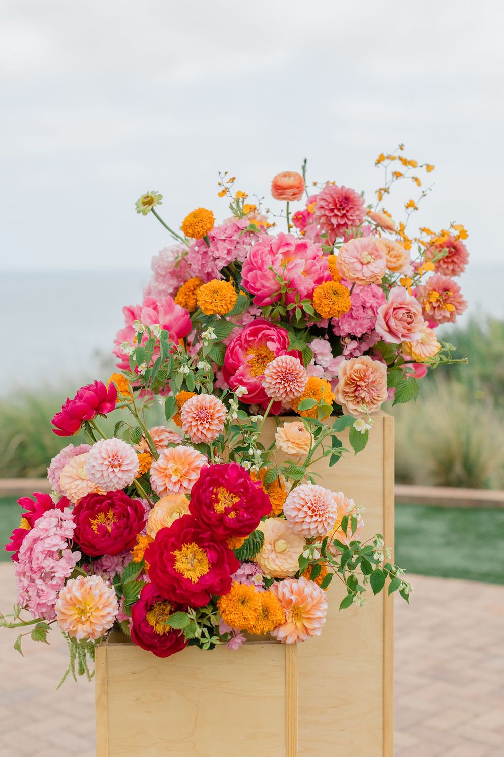 Vibrant pink, orange and coral dahlias and roses arranged in wooden box planters on an outdoor patio.