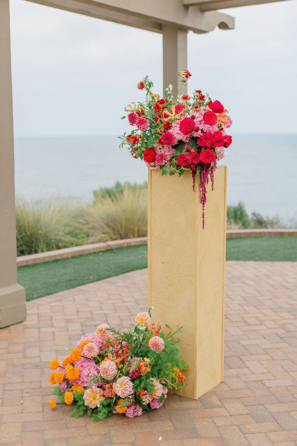 Outdoor patio with cream-colored planters filled with vibrant pink and orange flowers against an ocean view.