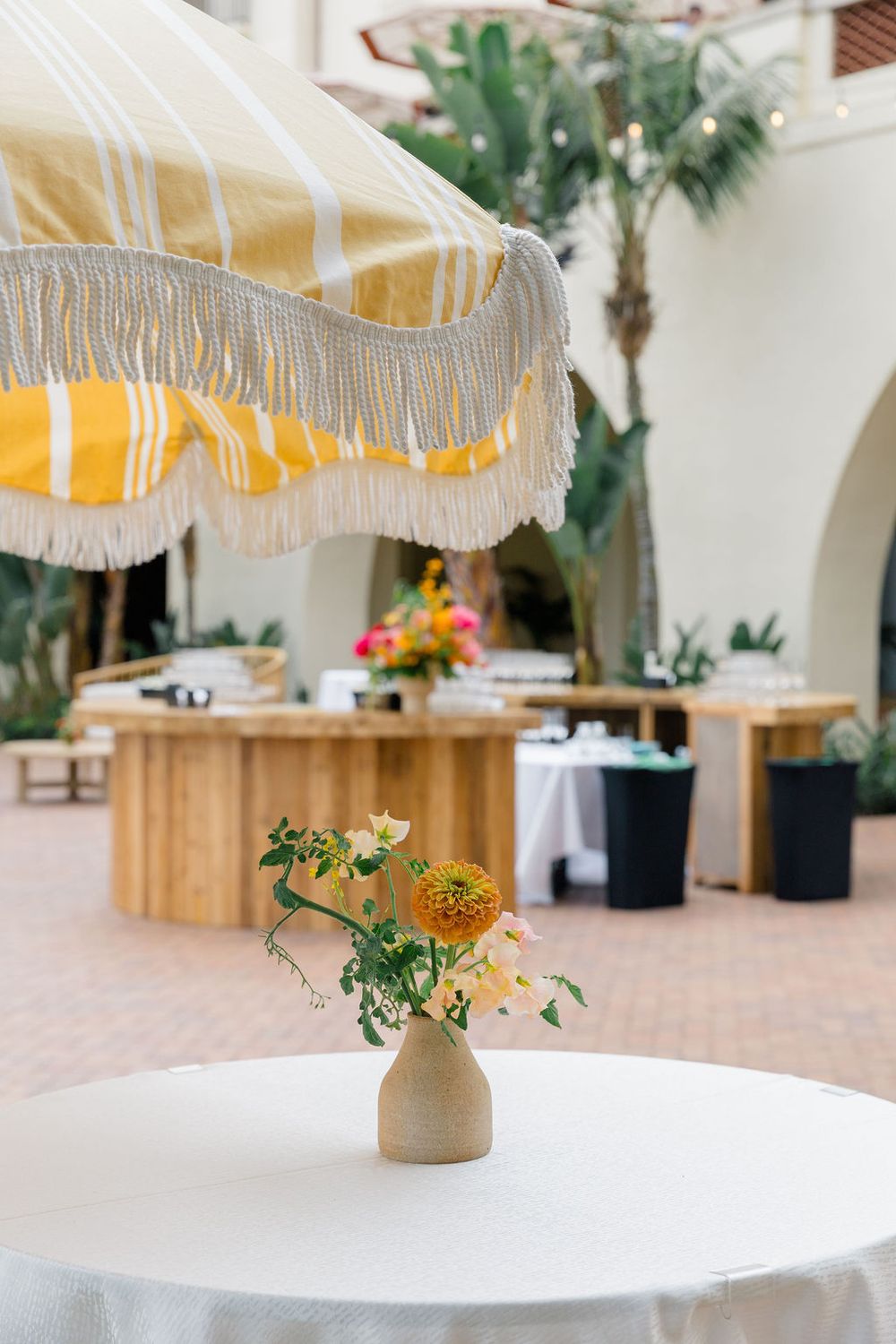Modern outdoor dining space with yellow fringed umbrella and minimalist floral centerpiece.