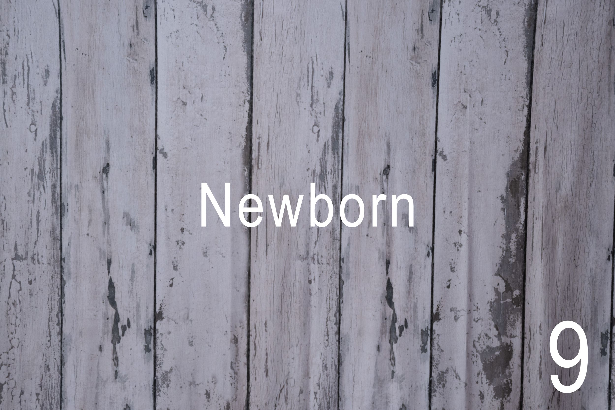 A newborn baby sleeps peacefully swaddled in white fabric against a rustic gray wooden background.