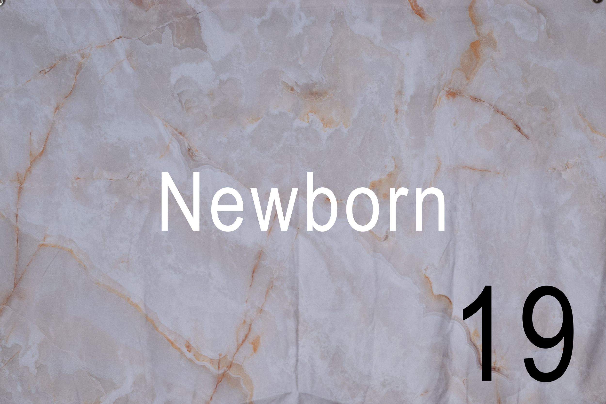 A small baby in a white onesie lies on a blanket with numbered milestone cards showing 19 weeks.