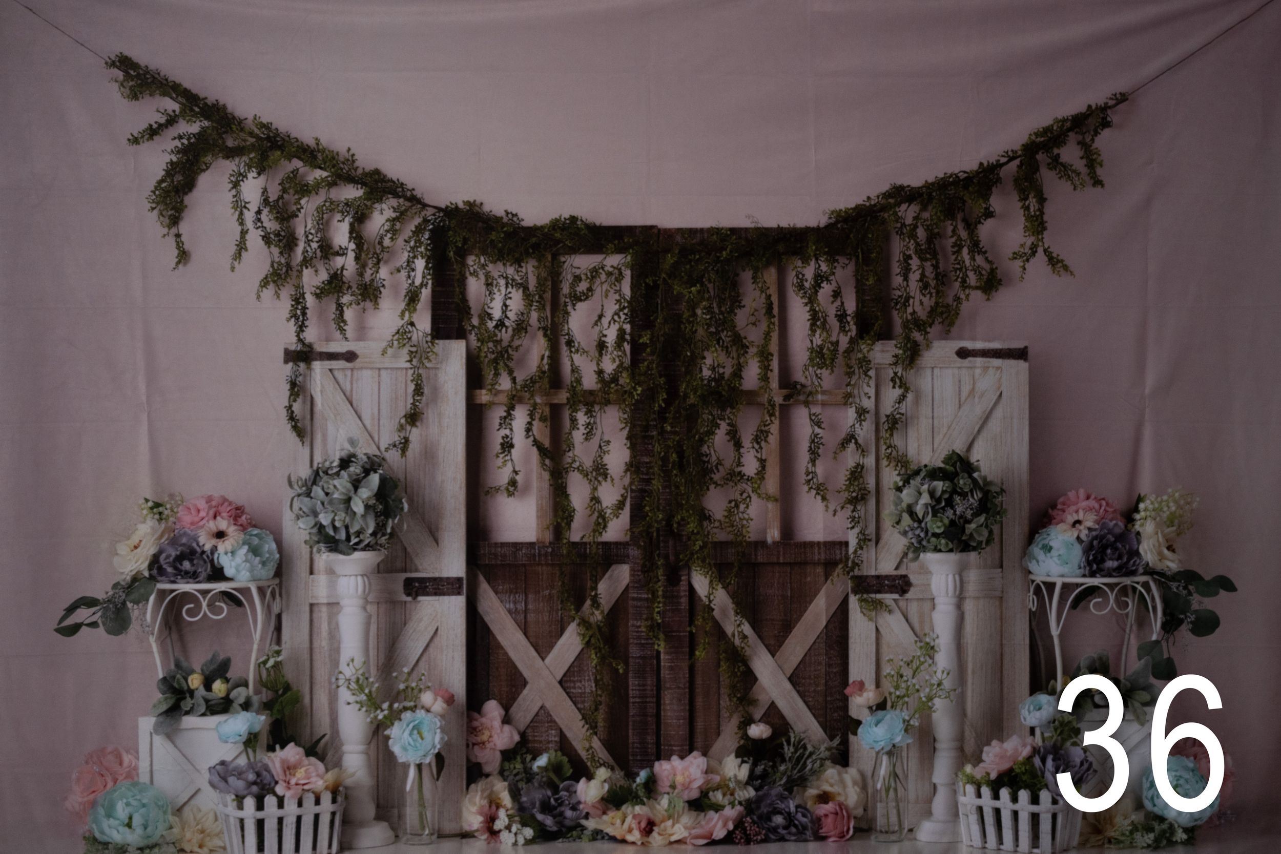 Rustic barn door backdrop with greenery garland and floral arrangements for a wedding ceremony setup.