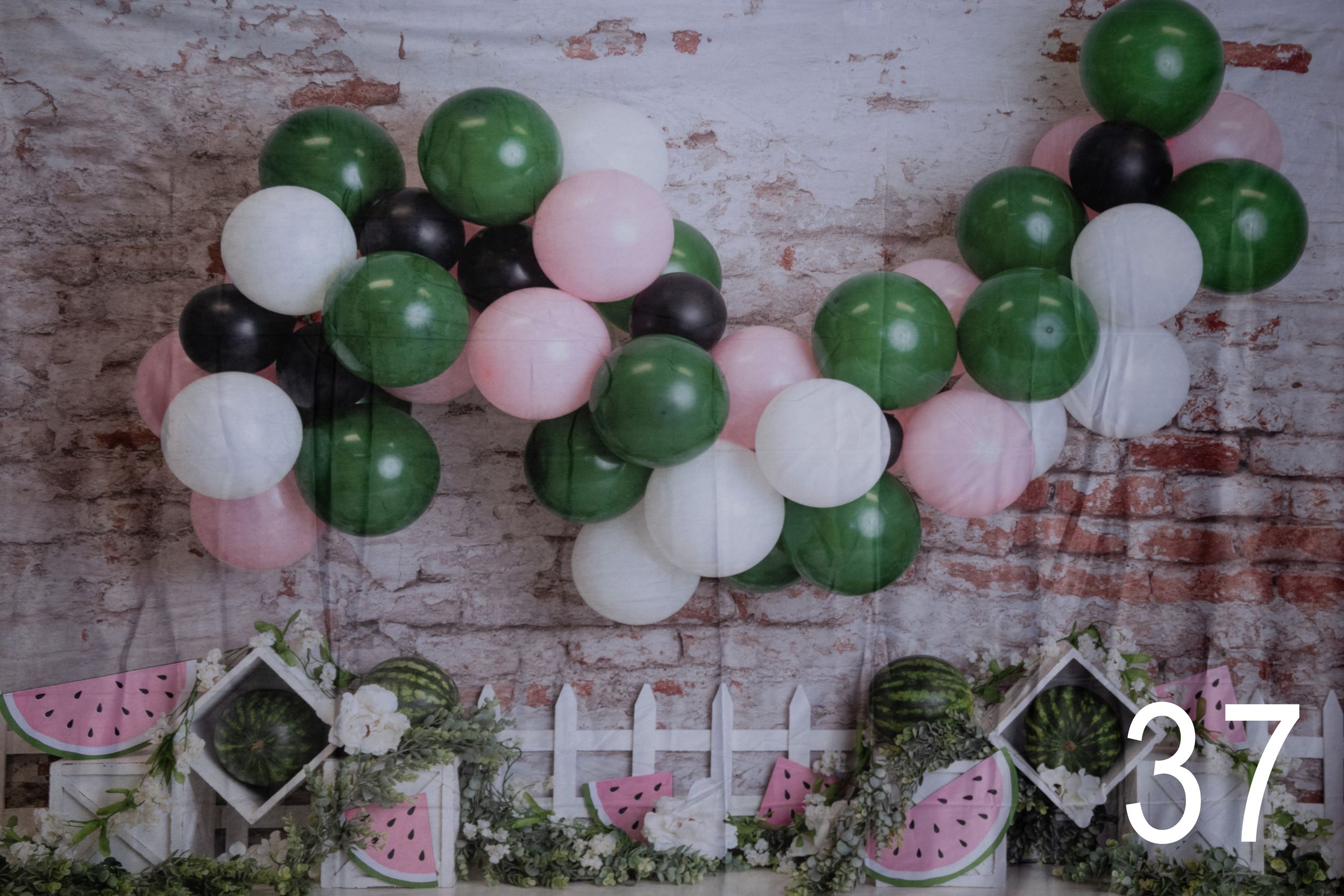 Pink, white and green balloon garland decoration against a distressed wall with floral accents.