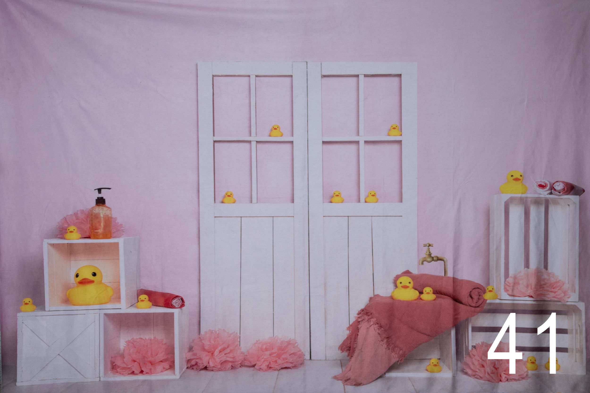 Pink and white baby nursery room setup with decorative doors, shelves, and yellow duck accents against a soft pink backdrop.