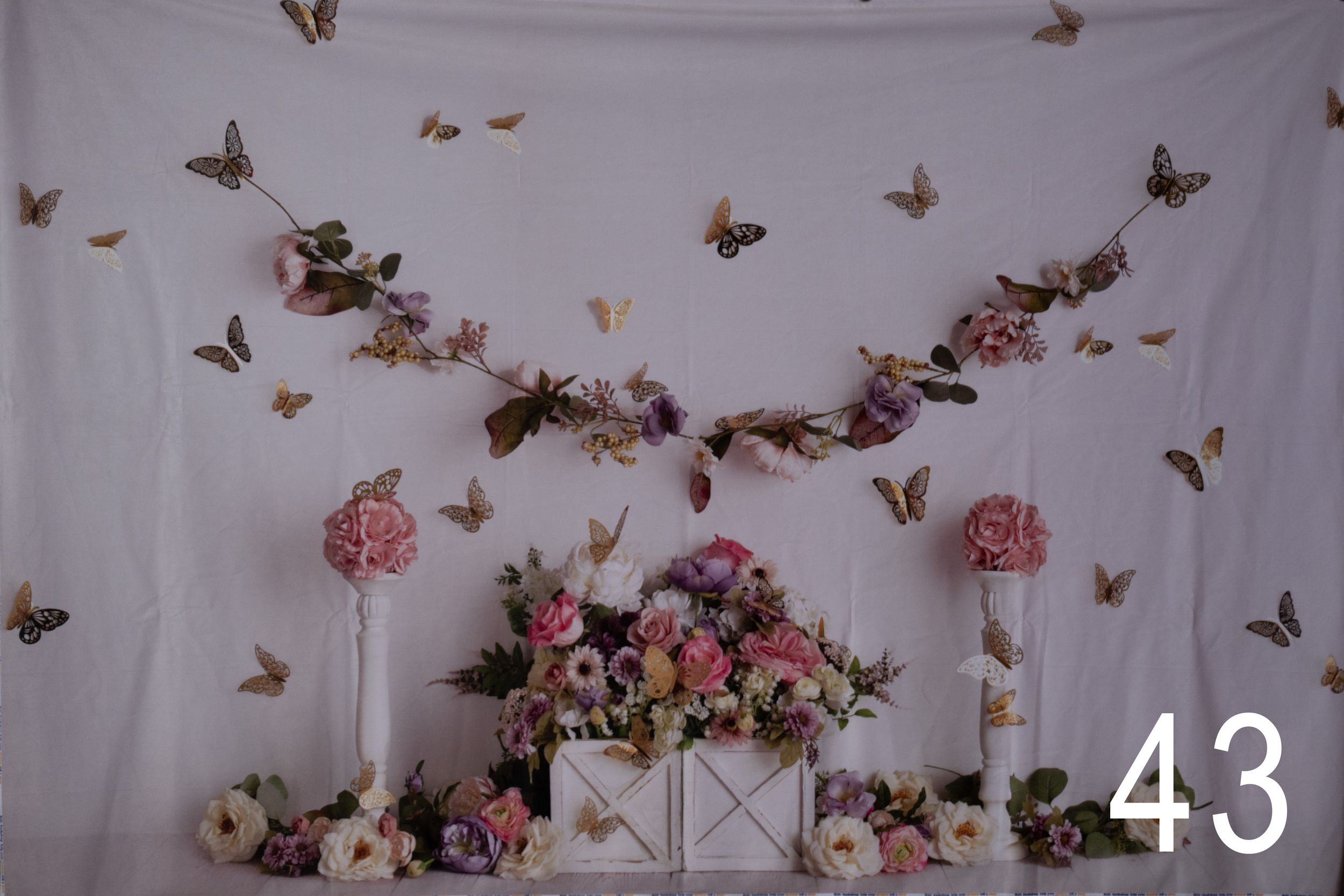 Pink floral arrangement with butterflies against white backdrop featuring tall candle holders and romantic garden decor.