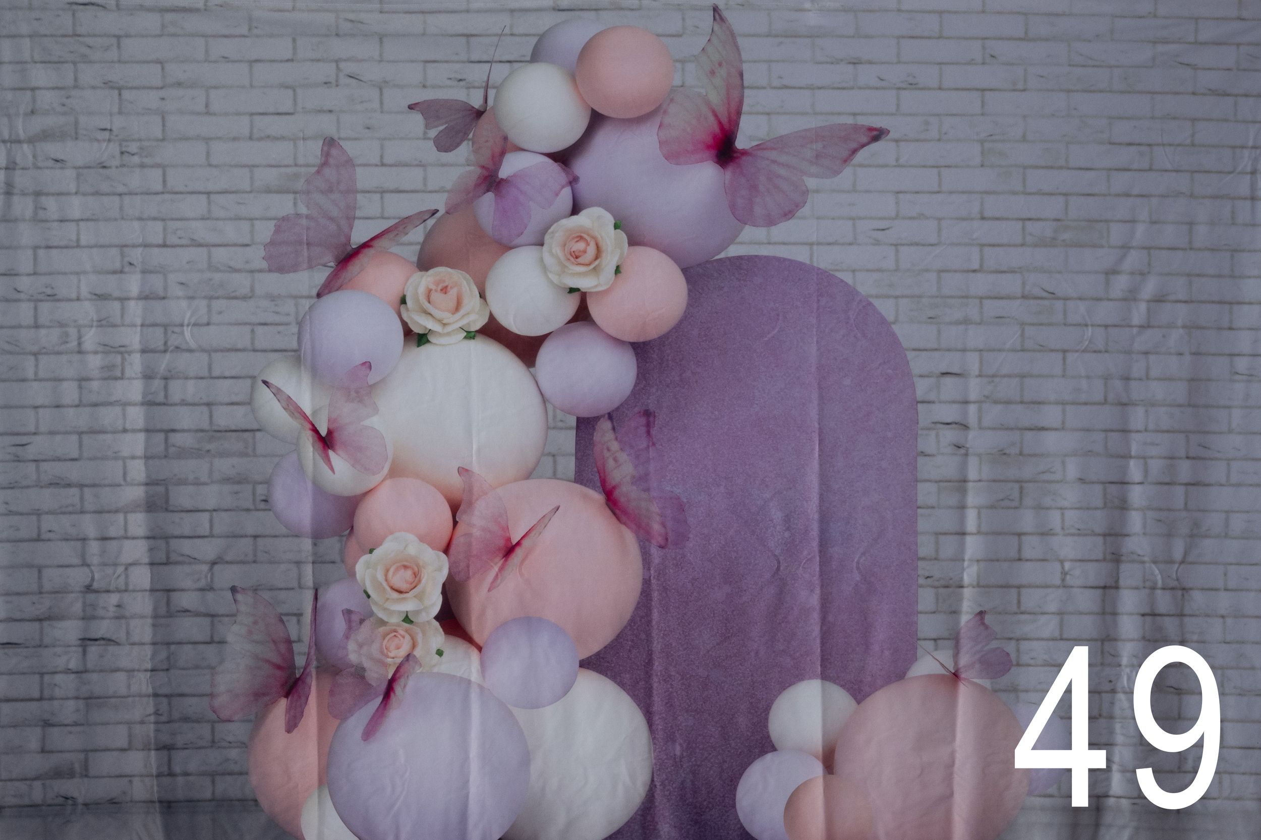 Elegant pastel balloon arch with pink and white balloons against a gray brick wall creates a romantic backdrop.