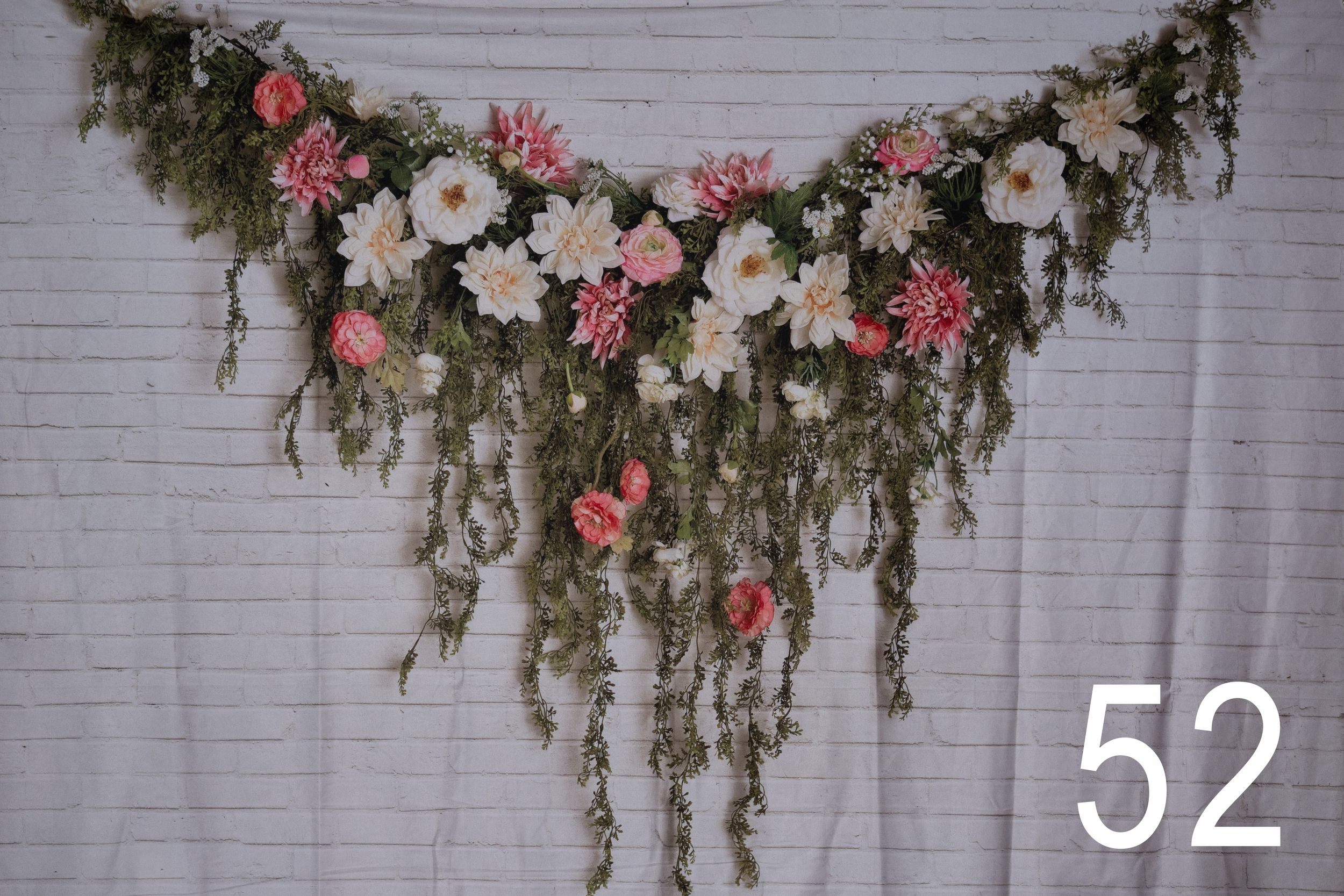 Floral garland with pink and white flowers hangs elegantly against a white brick wall backdrop.