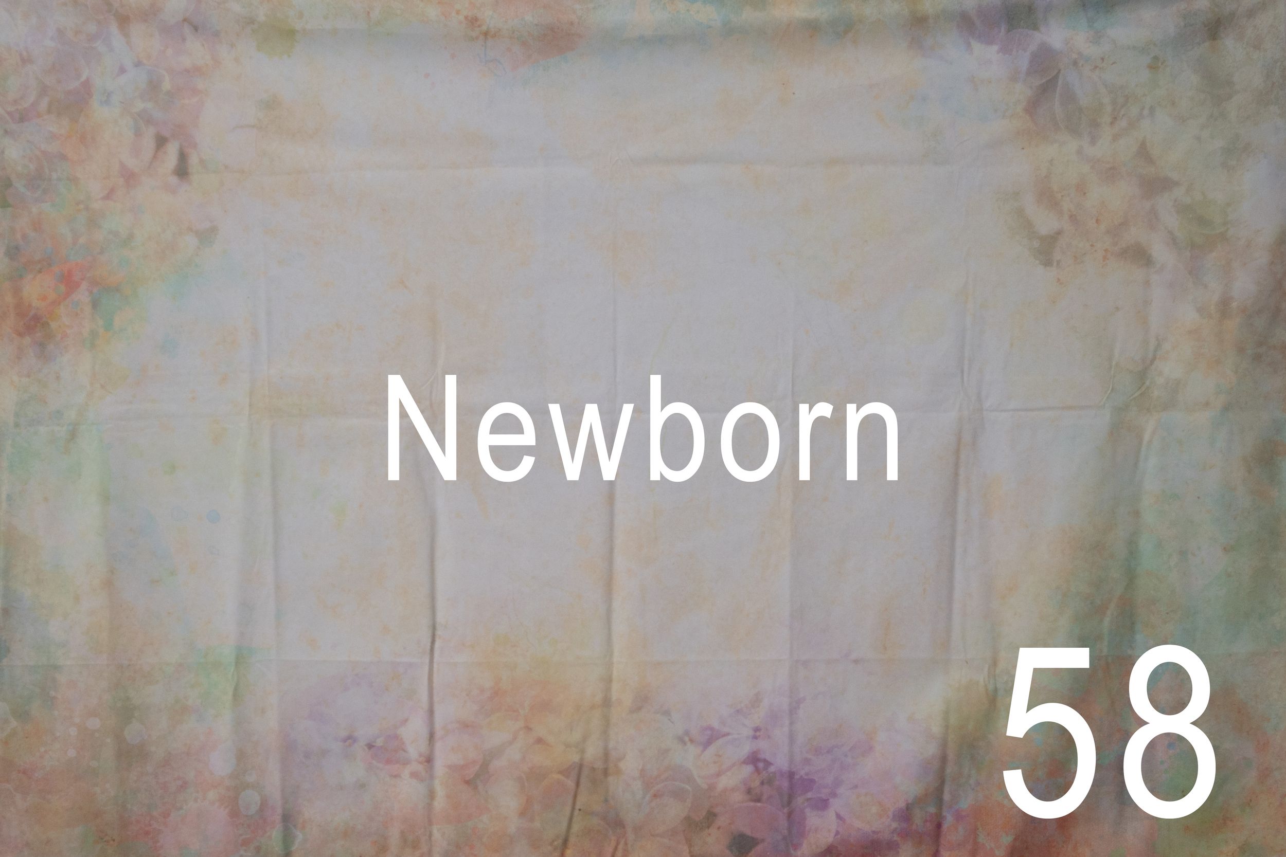 A newborn baby sleeps peacefully while wrapped in a soft white swaddle blanket against a textured beige background.