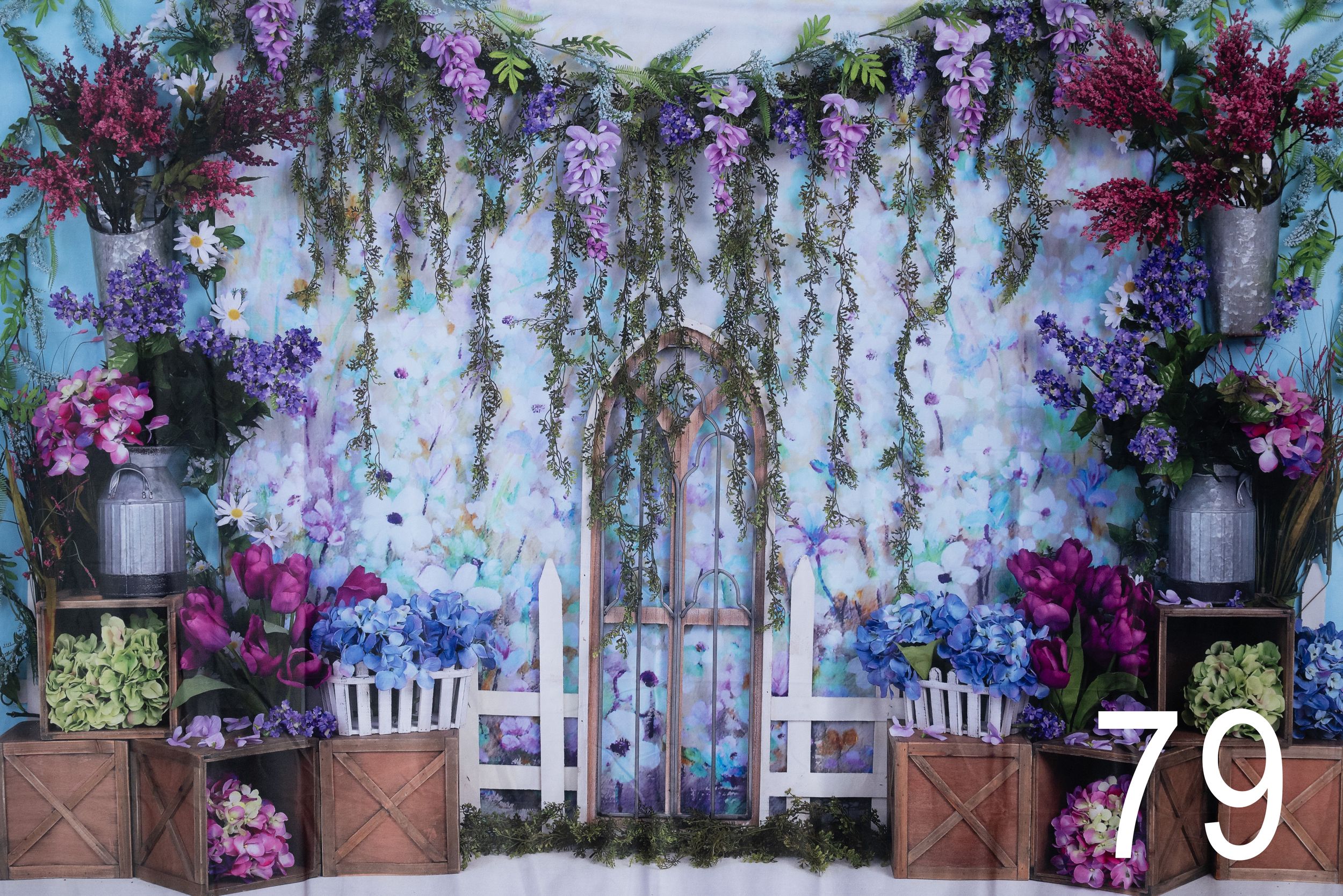 Romantic garden backdrop with hanging wisteria, purple flowers, and white chairs arranged for an elegant outdoor setting.