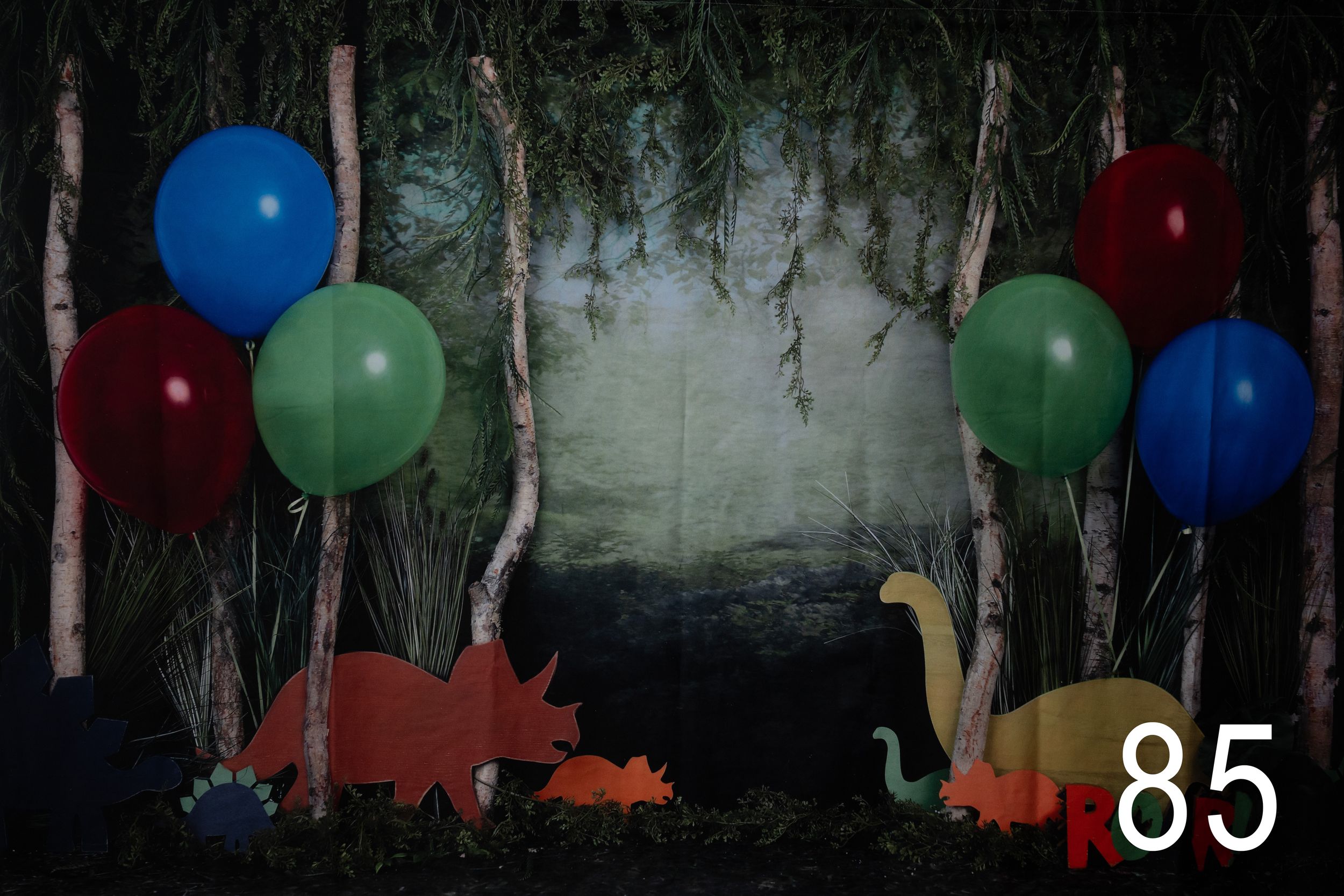 Colorful balloons float against a dark background with silhouettes of dinosaur decorations visible.