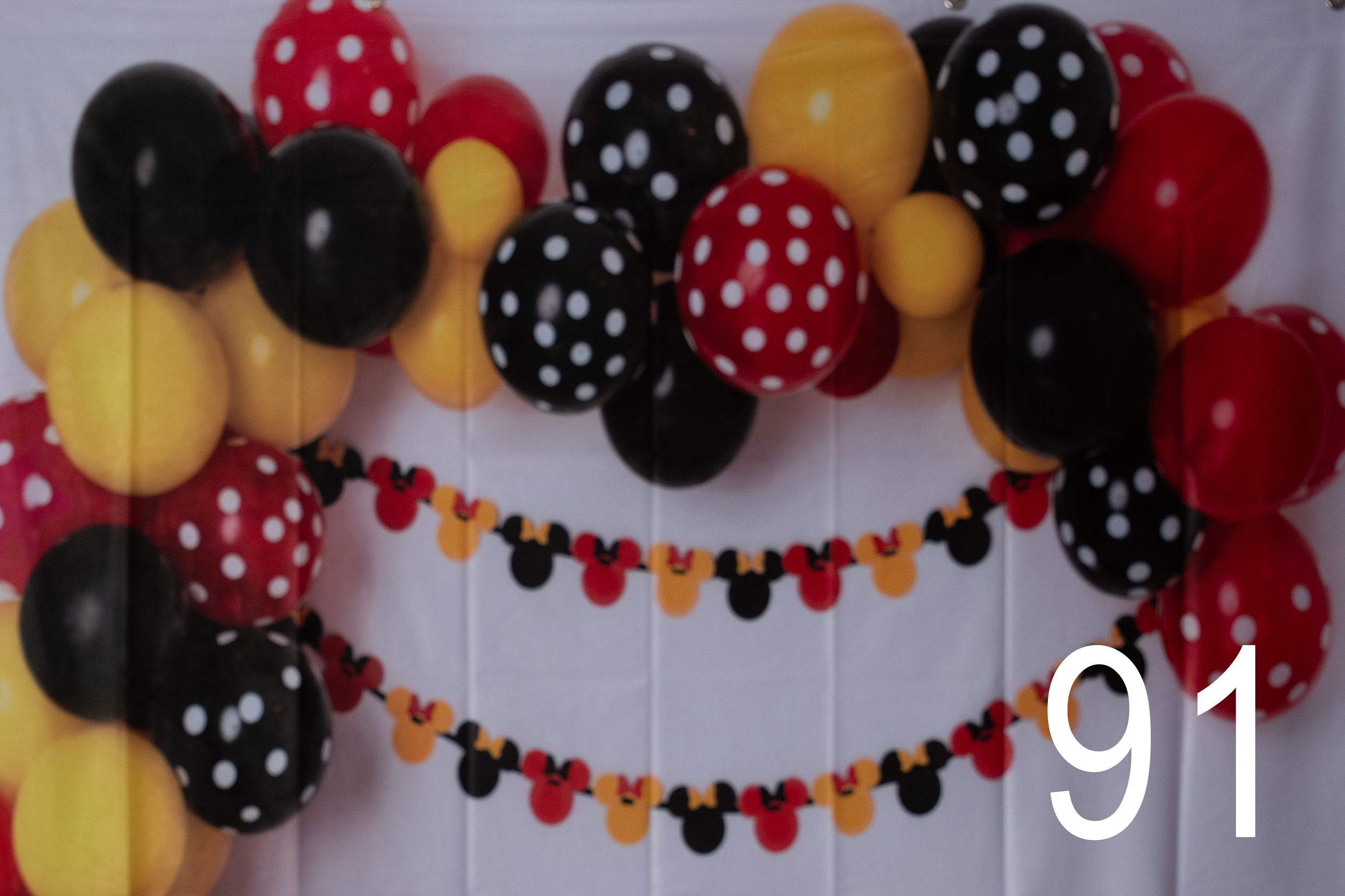 Red, black, and yellow polka dot balloons create a festive arch with Mickey Mouse themed party decorations.