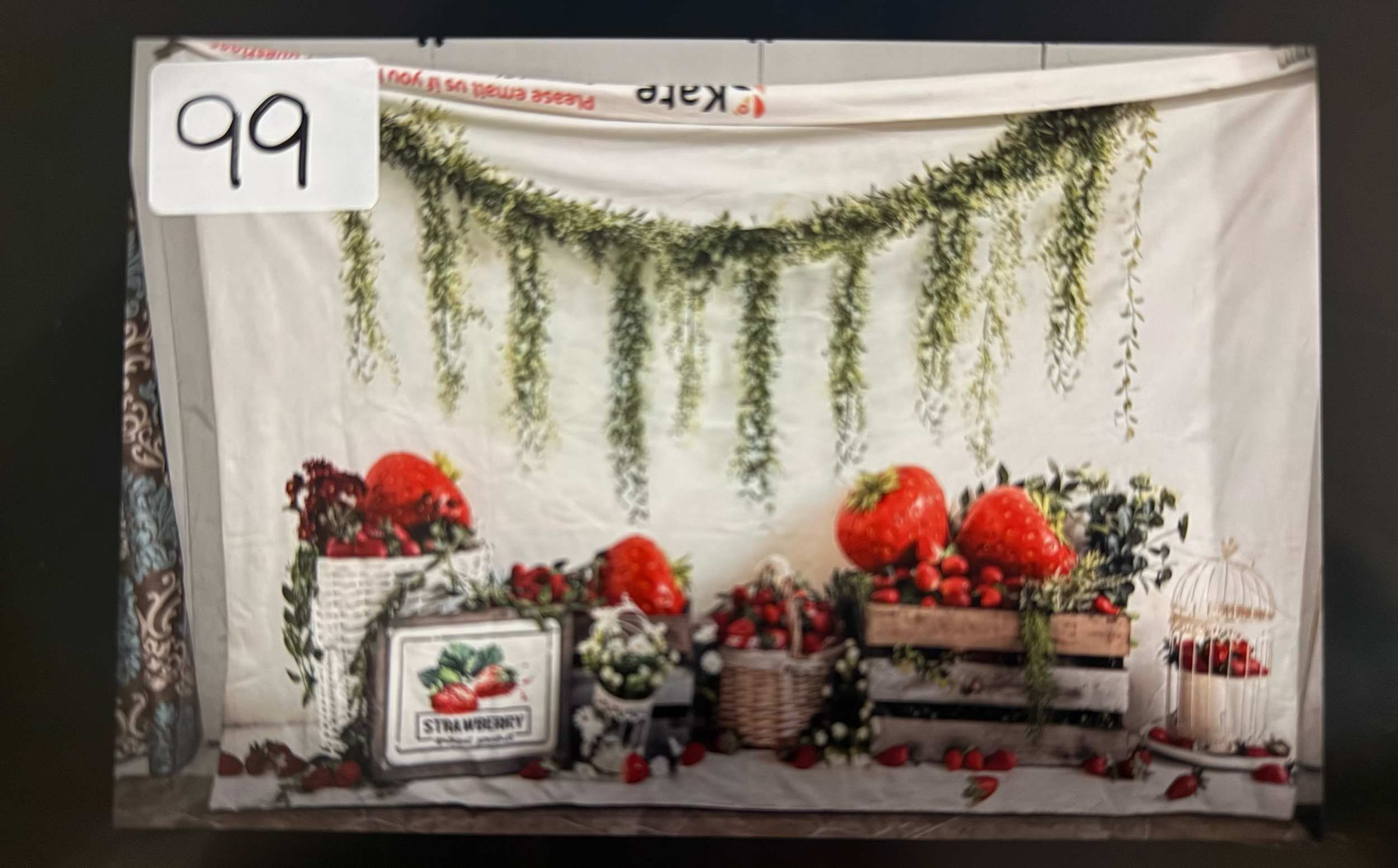 A rustic wedding venue setup with greenery garlands, wooden barrels, and red floral arrangements against white fabric backdrops.