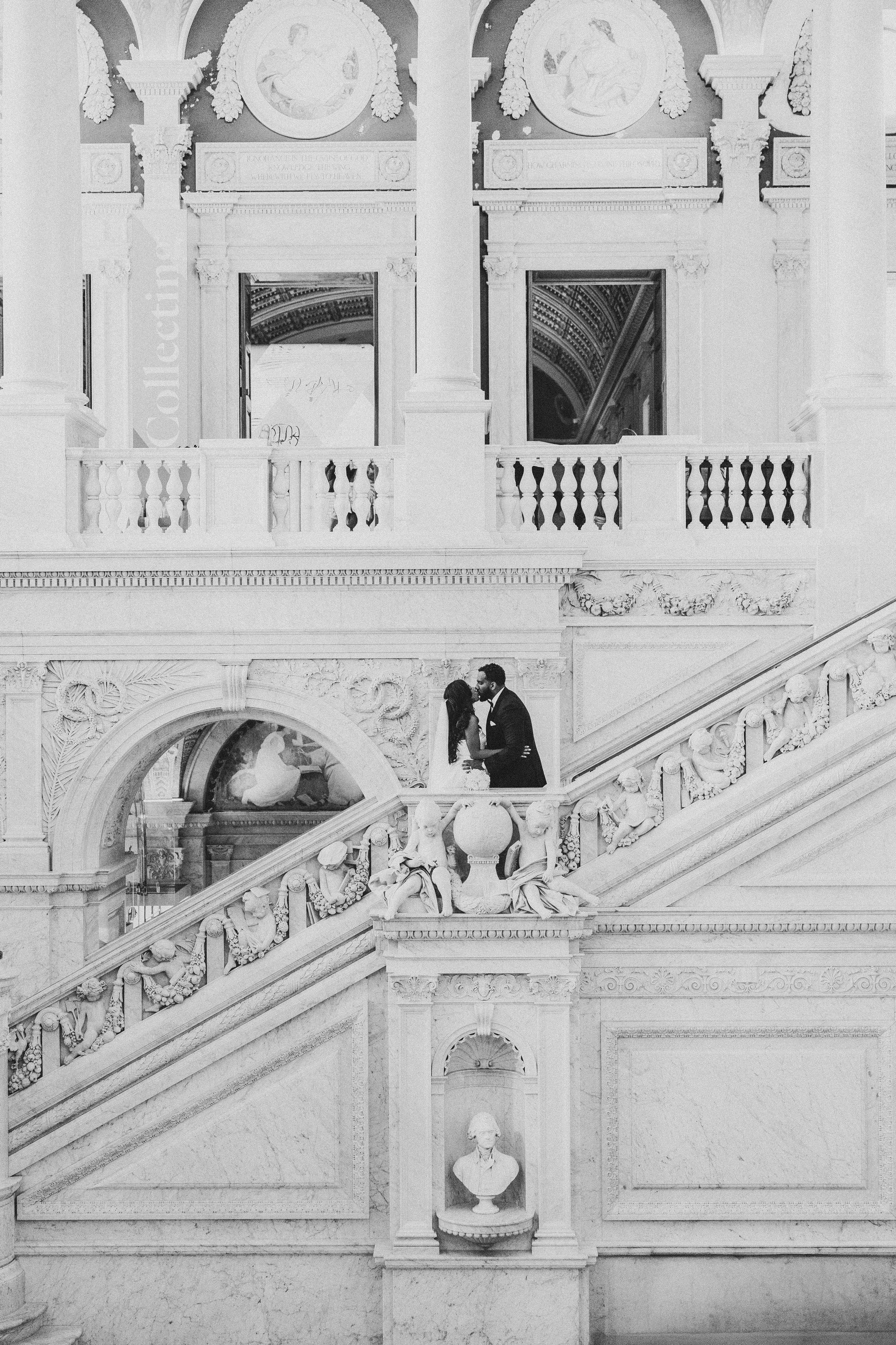 Black and white architectural detail of an ornate staircase with decorative balustrades and moldings in a grand interior.