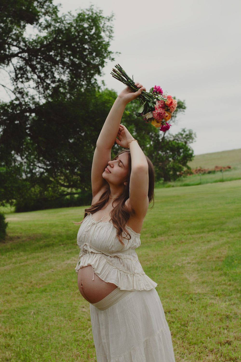 Woman in white dress dancing joyfully in a green field with flowers.