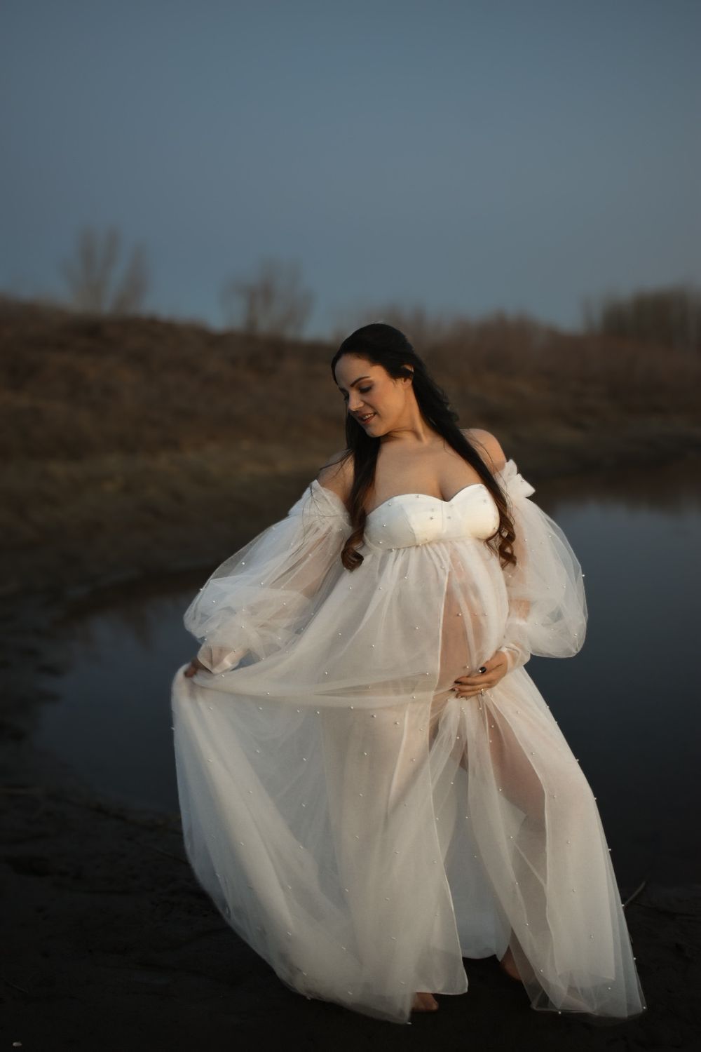 Artistic portrait session with billowing white fabric creating dreamy movement by the water.