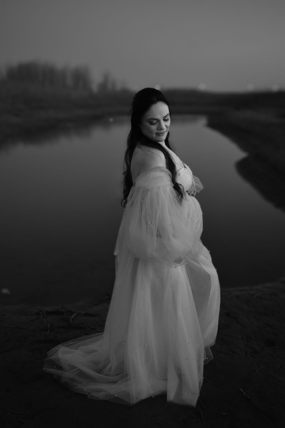 Dramatic black and white portrait series with flowing white dress near a serene lake.