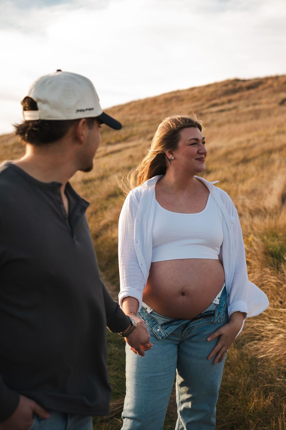 Expectant couple sharing intimate moments in golden grass field at sunset.