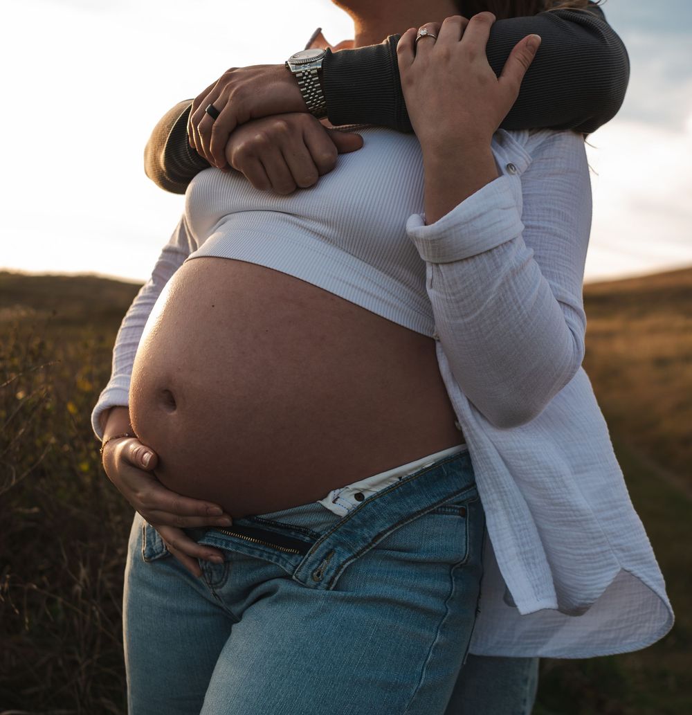 Maternity photoshoot capturing tender moments between couple in natural setting.
