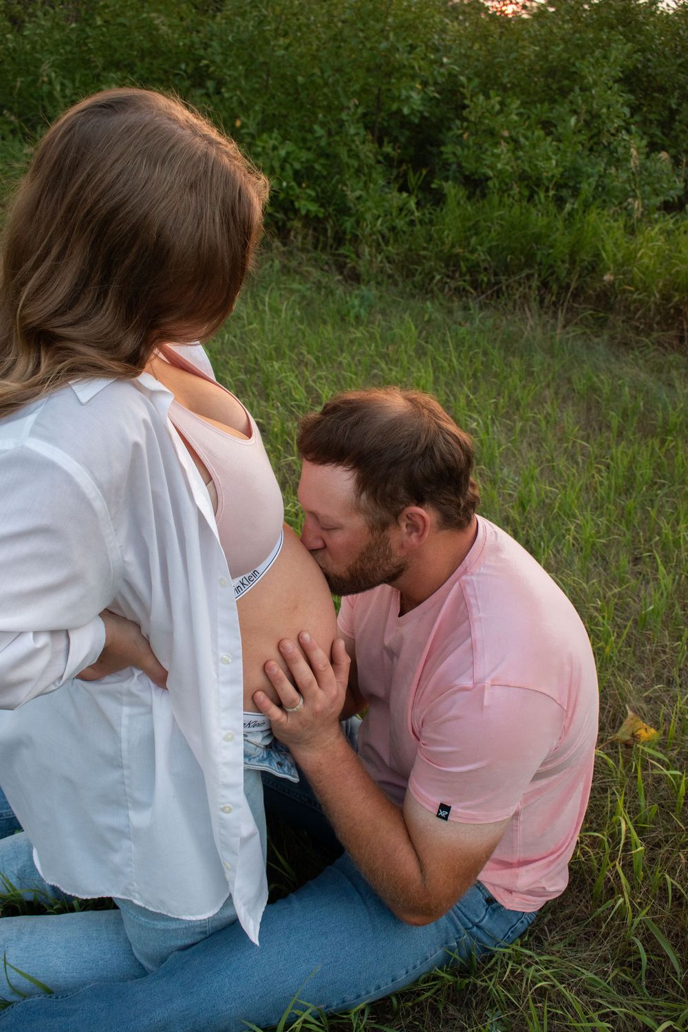 Intimate maternity moment captured between couple in outdoor setting at sunset.