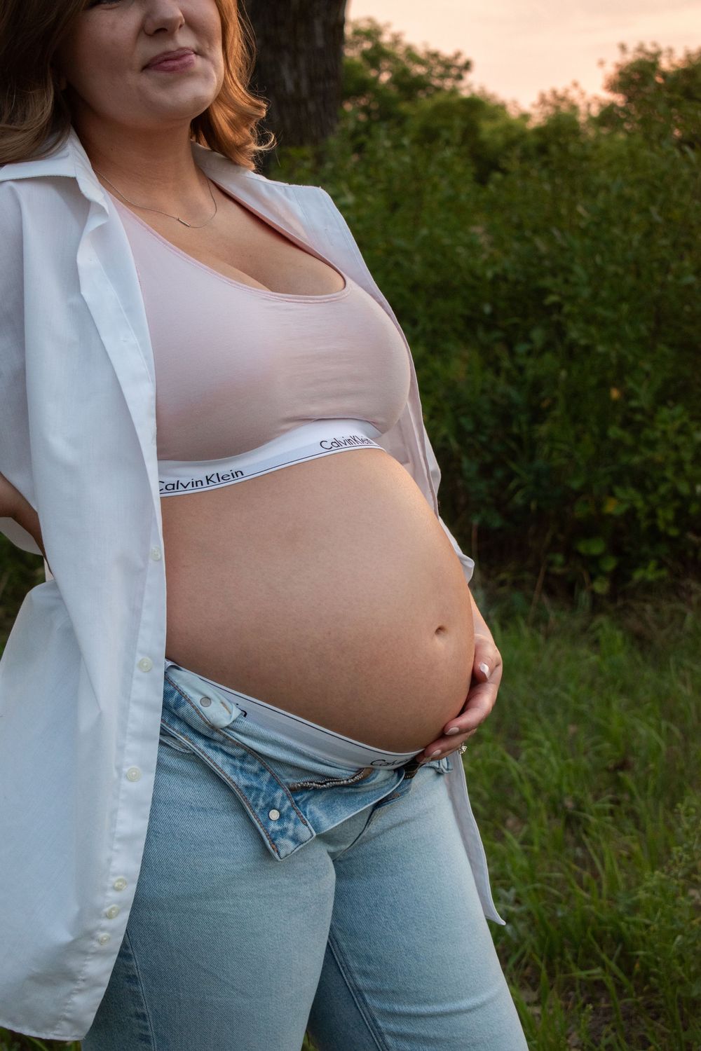 Casual maternity photo showing pregnant belly with white shirt and jeans in natural setting.