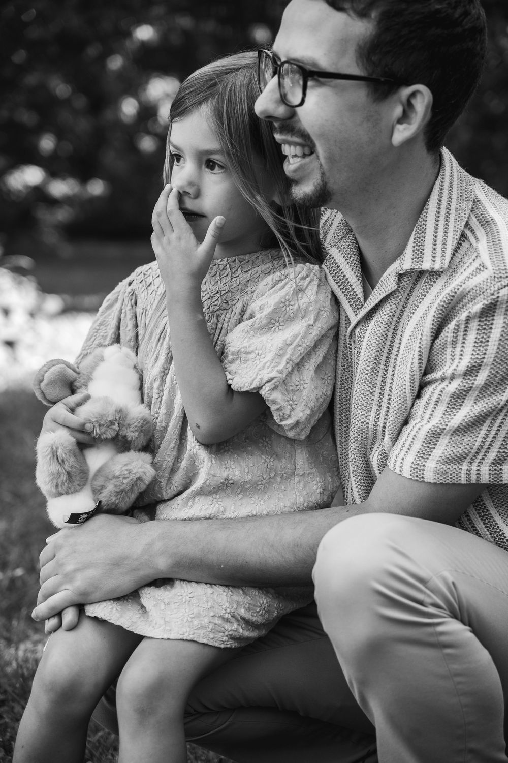 Black and white photo of a tender moment between parent and child sitting outdoors with a stuffed animal.