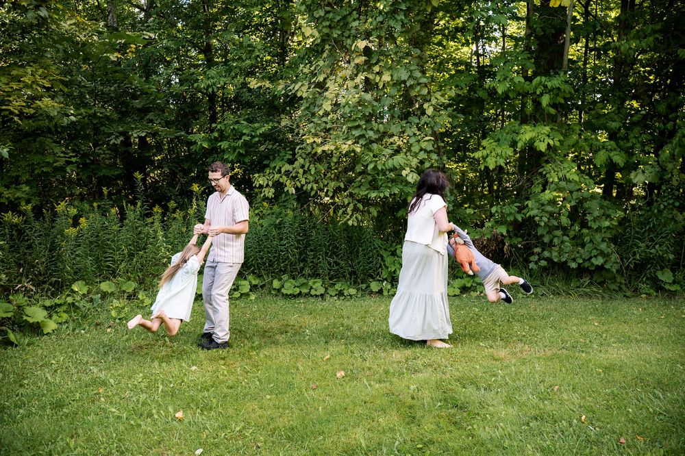 People in white outfits playing croquet on a lush green lawn bordered by trees and bushes.