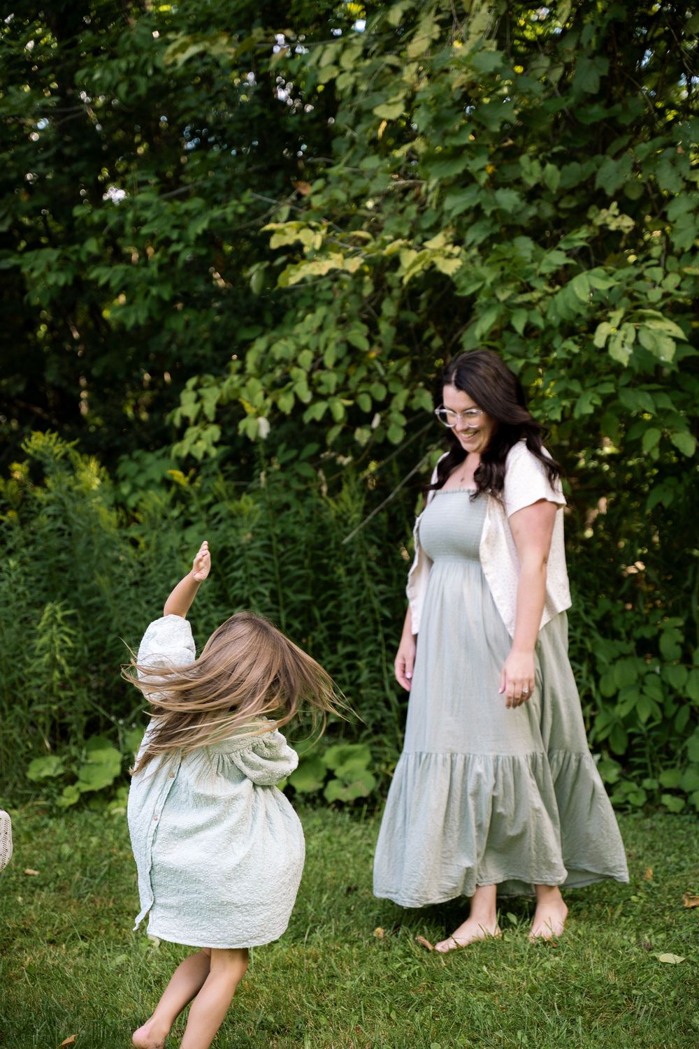 People in light colored dresses spinning and dancing on grass with trees in the background.