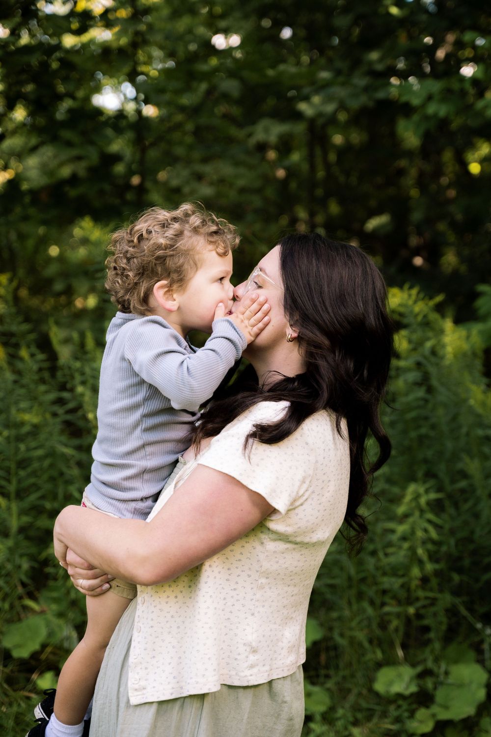 A tender moment of affection and embrace captured in a natural outdoor setting with green foliage in the background.