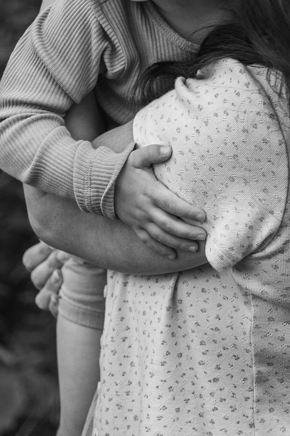 A series of black and white photos showing gentle hands holding and embracing a small baby in a polka dot onesie.