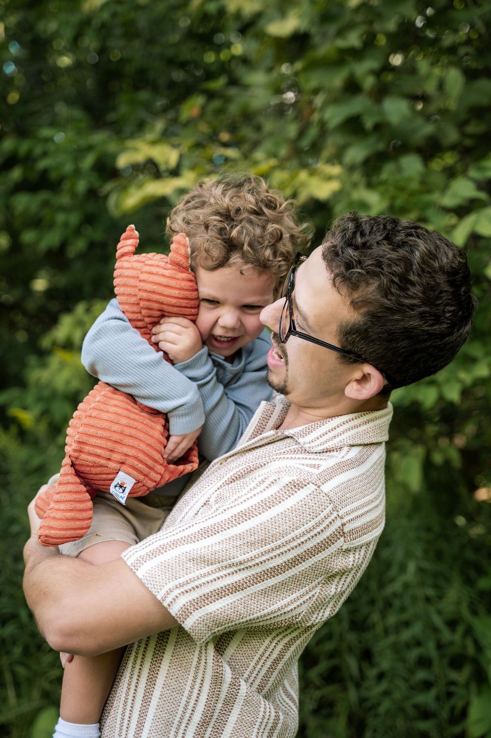 Playful moment of joy and laughter between parent and child in a lush green outdoor setting.