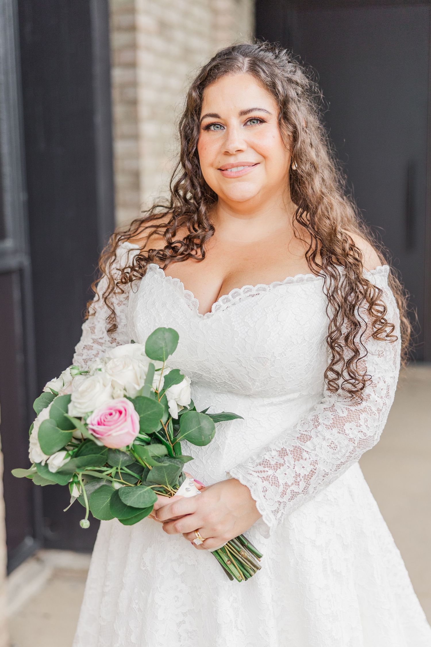 Bride in lace sleeve wedding gown holds classic white and pink rose bouquet.