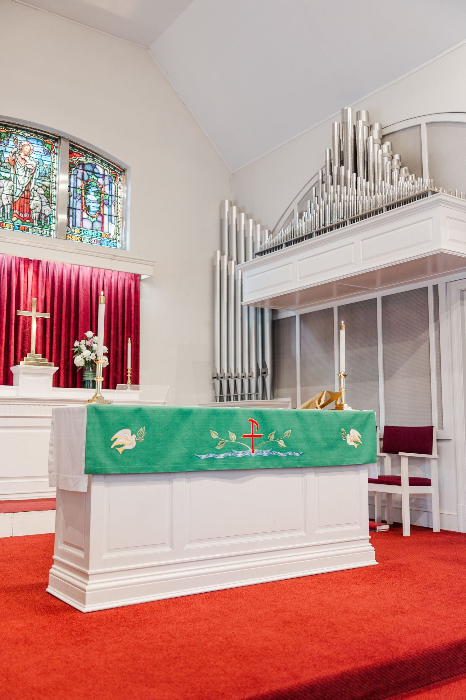 White church altar with organ pipes and red carpet showcases different angles of the sacred space.
