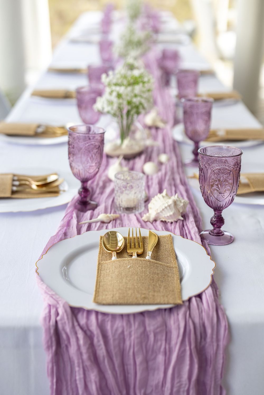 Elegant table setting with purple chiffon runner, gold flatware, and ornate violet glassware on white linens.