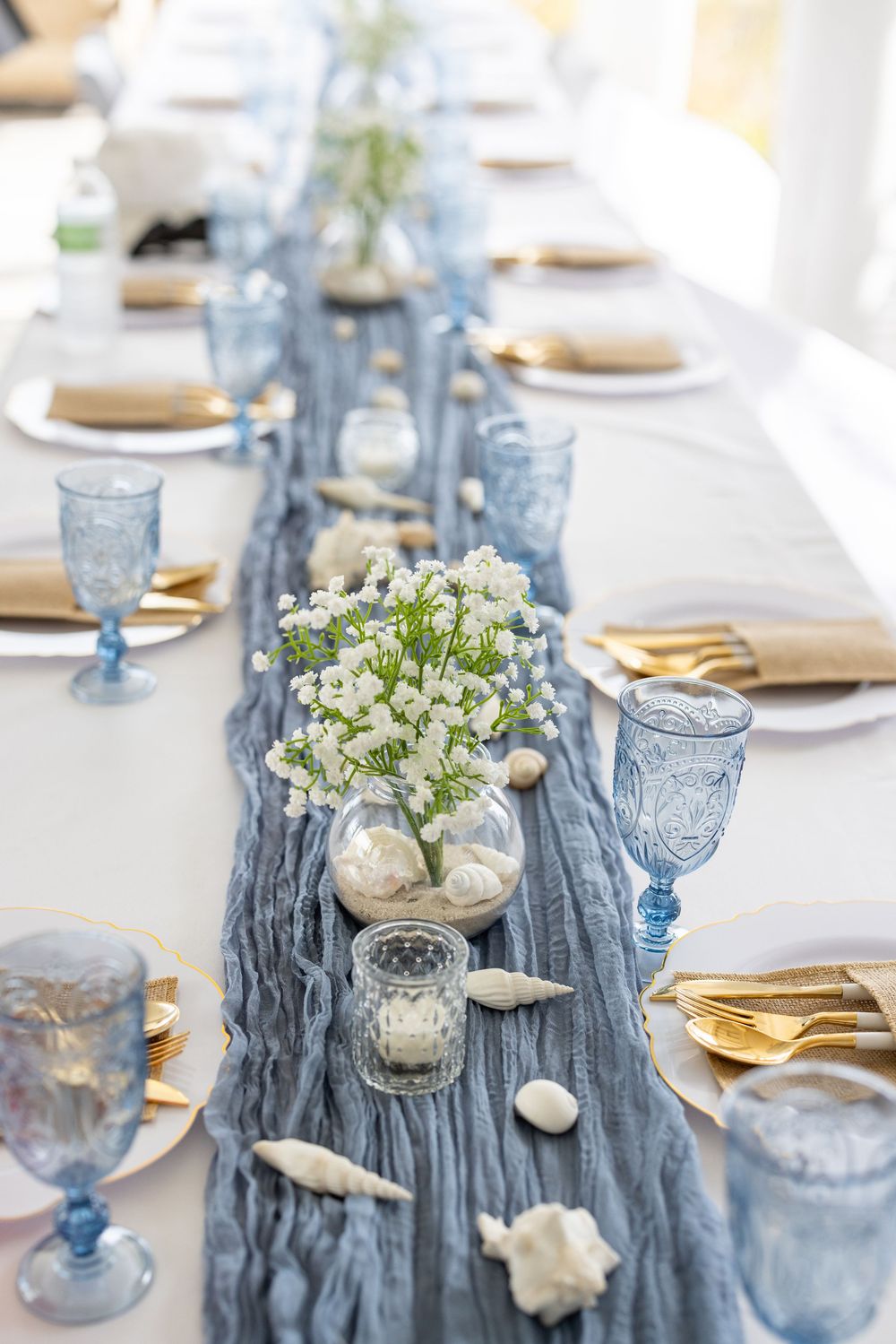 Wedding table decor with dusty blue chiffon runner, gold cutlery, and vintage-style blue glassware.