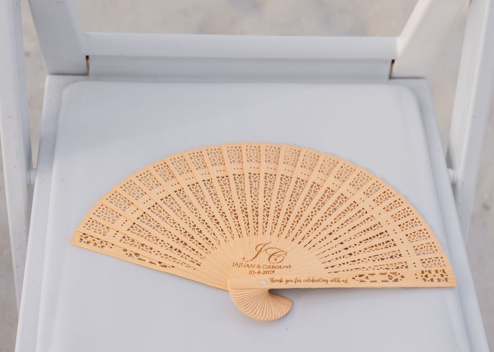 A decorative wooden folding fan with intricate carved patterns displayed on a white surface.