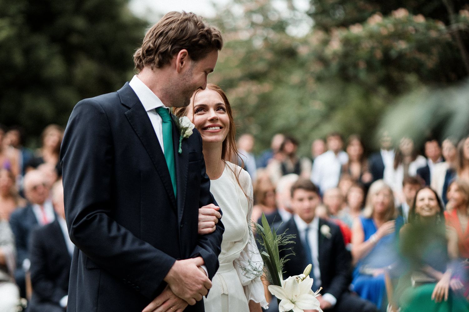 Wedding couple sharing a joyful moment surrounded by smiling guests during an outdoor ceremony.