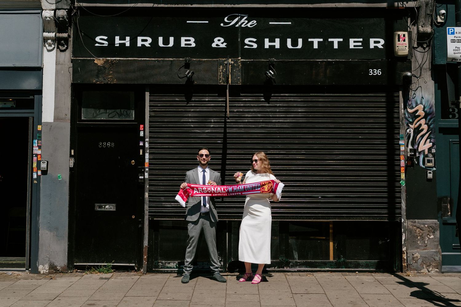 Couple holding Arsenal scarves outside The Shrub & Shutter bar in London on their wedding day.