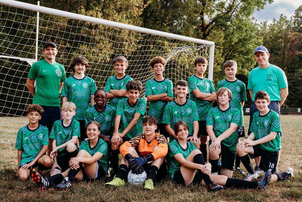 Soccer team in matching green jerseys poses together in front of goal net on sunny field.