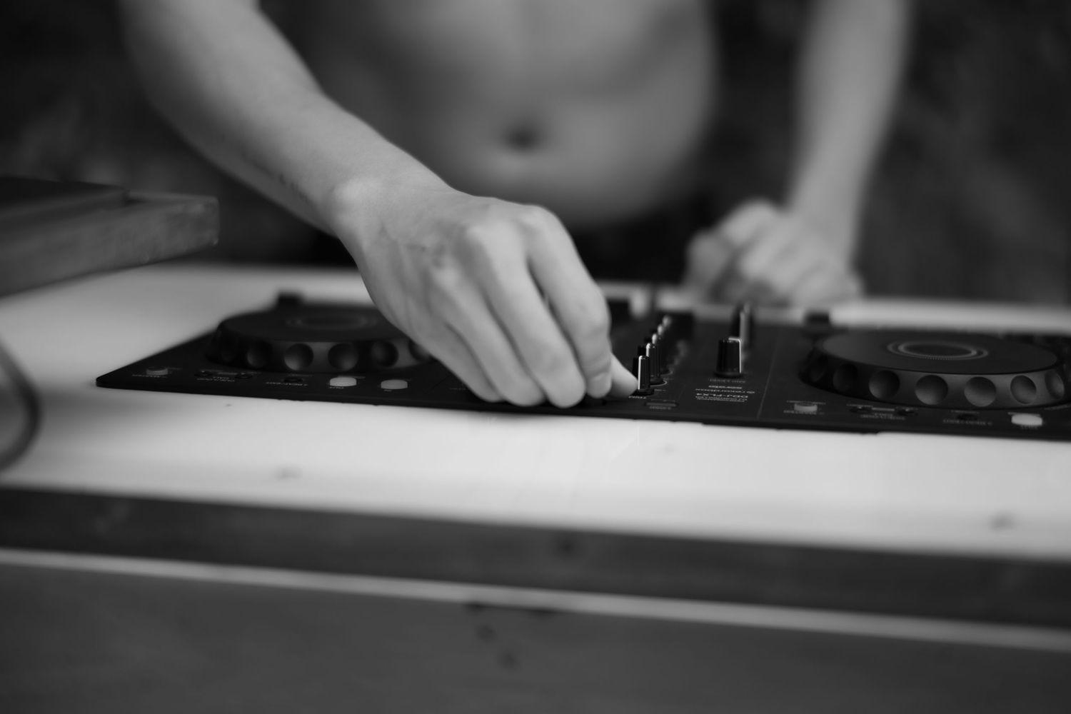 Black and white close-up of DJ hands adjusting mixer controls at outdoor wedding reception.