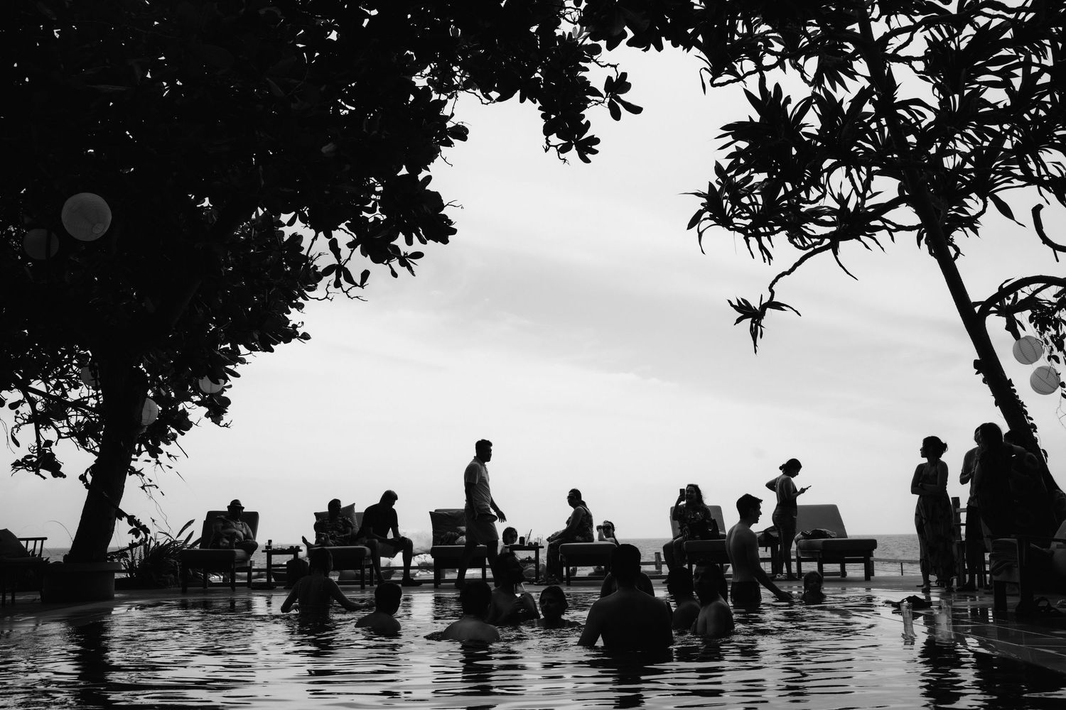 Silhouette of people gathered at a tropical infinity pool overlooking the ocean at dusk.
